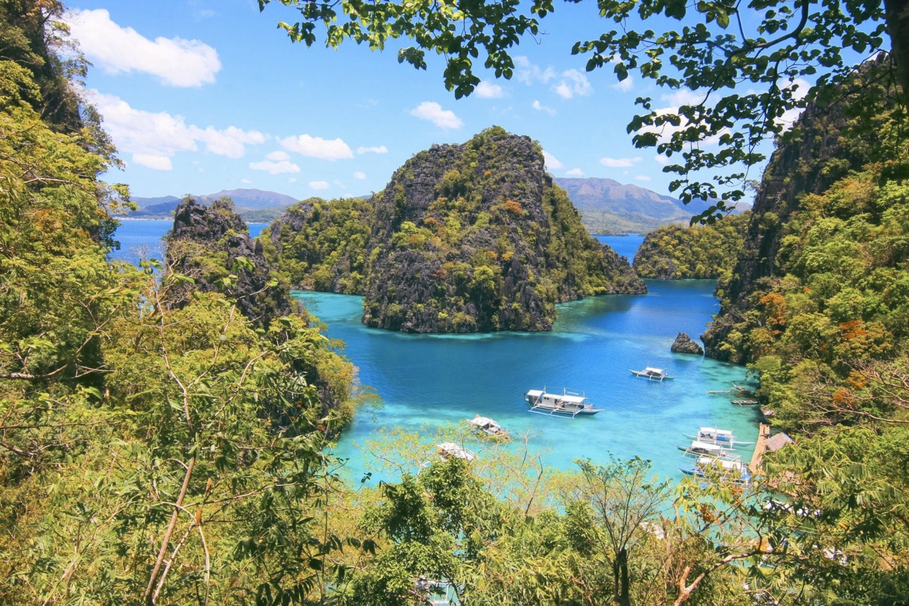 Boote in einer türkisfarbenen Lagune zwischen bewaldeten Felsen bei Coron