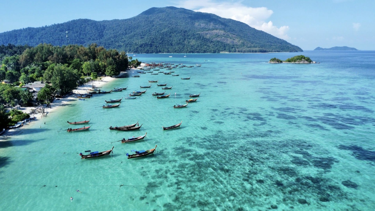 Perahu di air biru kehijauan di depan pantai Koh Lipe