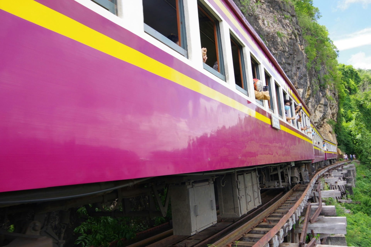 Kereta penumpang berwarna merah muda dan kuning melaju di sepanjang tebing batu