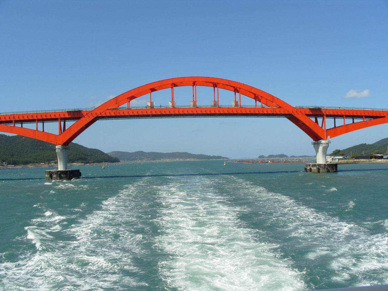 Blick vom Heck einer Fähre auf eine rote Bogenbrücke